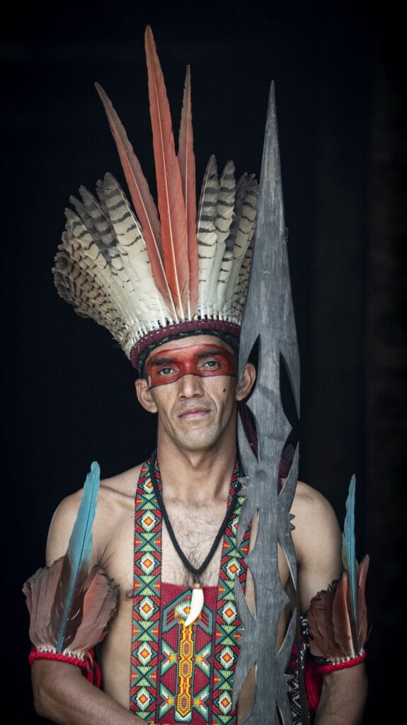 Hombre puyanawa con tocado de plumas, pintura facial roja y lanza