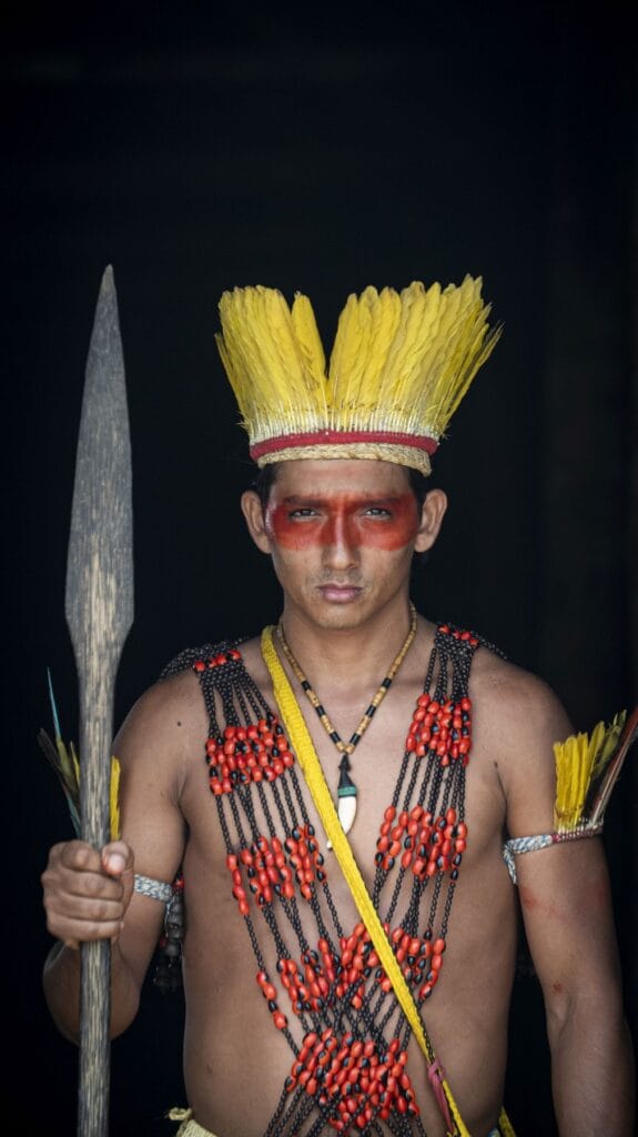 Joven puyanawa con tocado de plumas amarillas, pintura facial y lanza