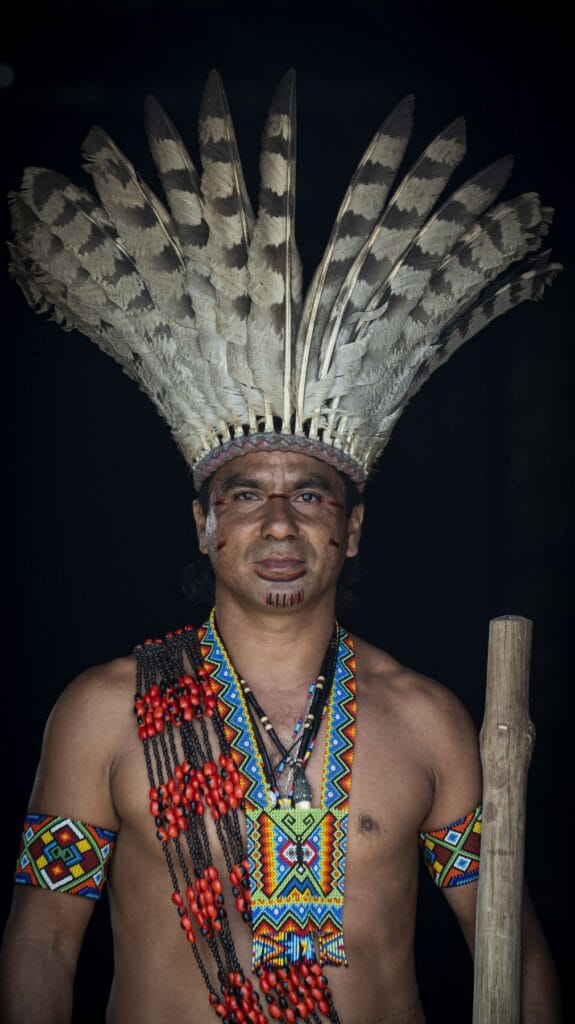 Hombre puyanawa con gran tocado de plumas moteadas y adornos de semillas rojas