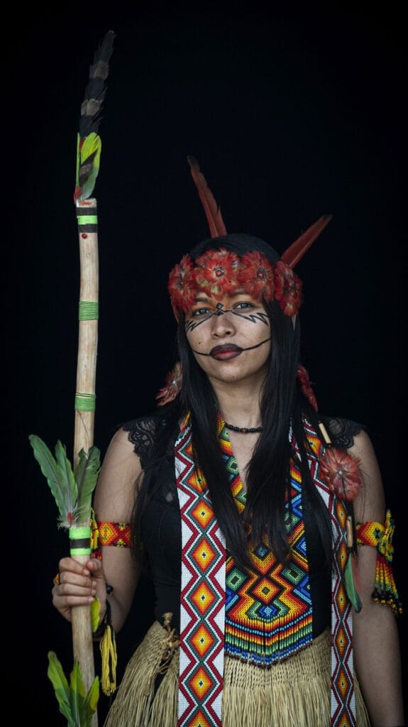 Mujer puyanawa con tocado rojo, pintura facial y chaleco de abalorios de colores