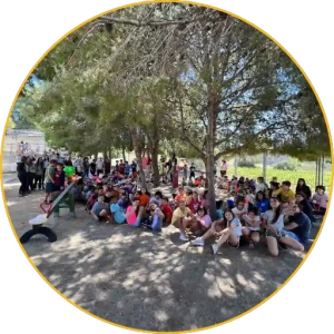 Large group of students sitting in the shade of the trees in the playground