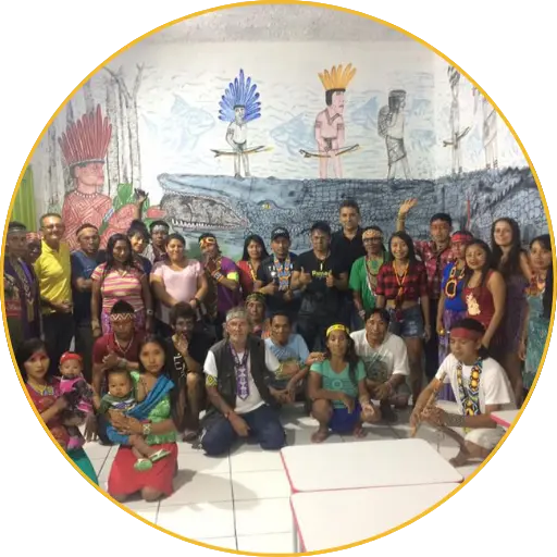 Numeroso grupo de personas indígenas y colaboradores posando ante un mural con figuras indígenas y un caimán