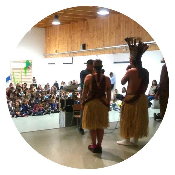 Puwe und Vari Puyanawa in traditioneller Kleidung vor den in der Turnhalle versammelten Schülerinnen und Schülern