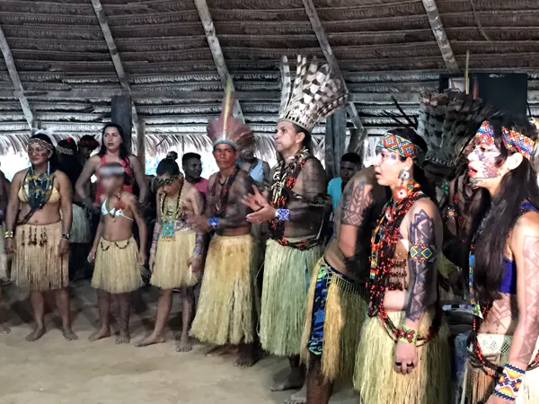 Mujeres y hombres Puyanawa con faldas de paja cantan en fila en la maloca