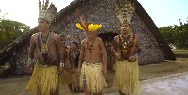 Puwe y otros miembros de la comunidad bailan con tocados de plumas frente a la maloca