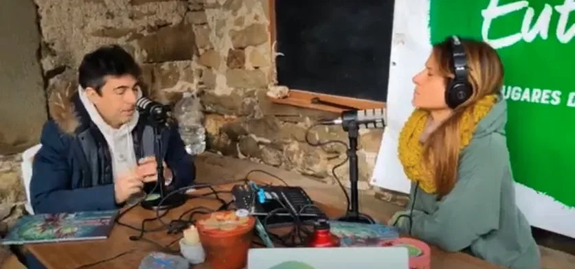Adolf Sanz y una presentadora conversan ante los micrófonos durante la grabación dthe Eutopías podcast; sobre la mesa, el libro del cuento
