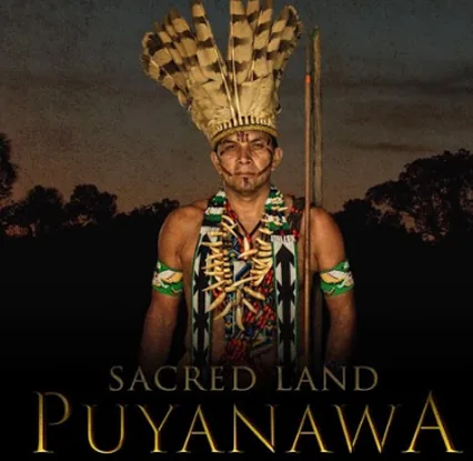 Cartel del documental «Sacred Land Puyanawa»: un hombre Puyanawa con penacho de plumas y lanza al anochecer