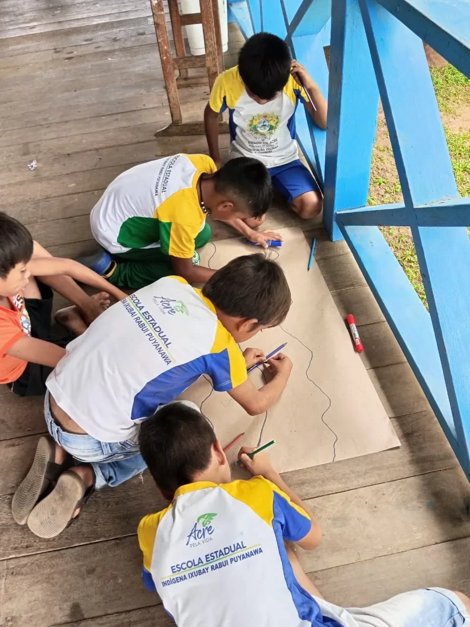 Nens i nenes puyanawa, amb uniforme escolar, dibuixen a terra sobre cartolines durant el taller