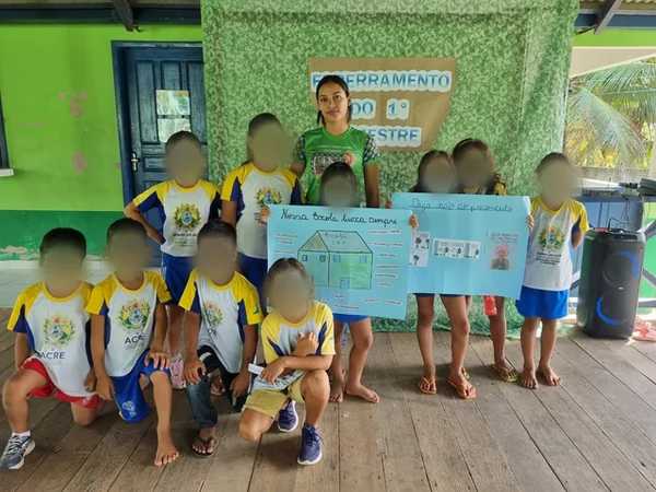 Kinder der Escola Ixubãy in Schuluniform posieren mit ihren Plakaten neben einer jungen Pädagogin