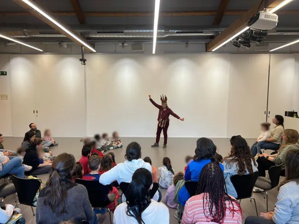La narradora, de pie en el centro de la sala, gesticula ante el público infantil y las familias