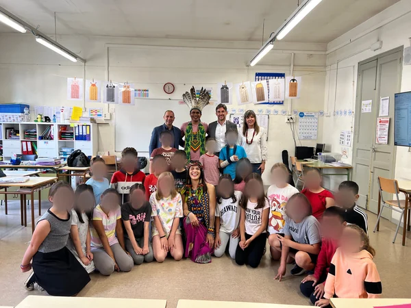 Kinder und Lehrkräfte einer katalanischen Schule posieren im Klassenzimmer als Gruppe mit zwei Gästen der Puyanawa