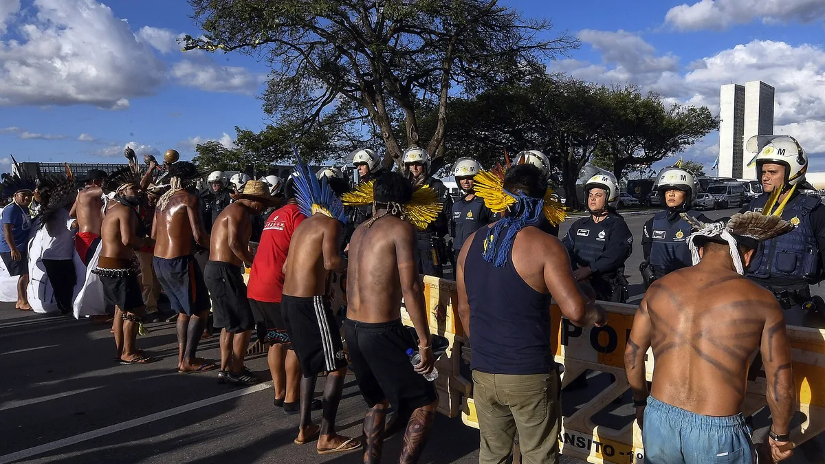 Personas indígenas frente a un cordón de policías con cascos y escudos en una avenida de Brasilia