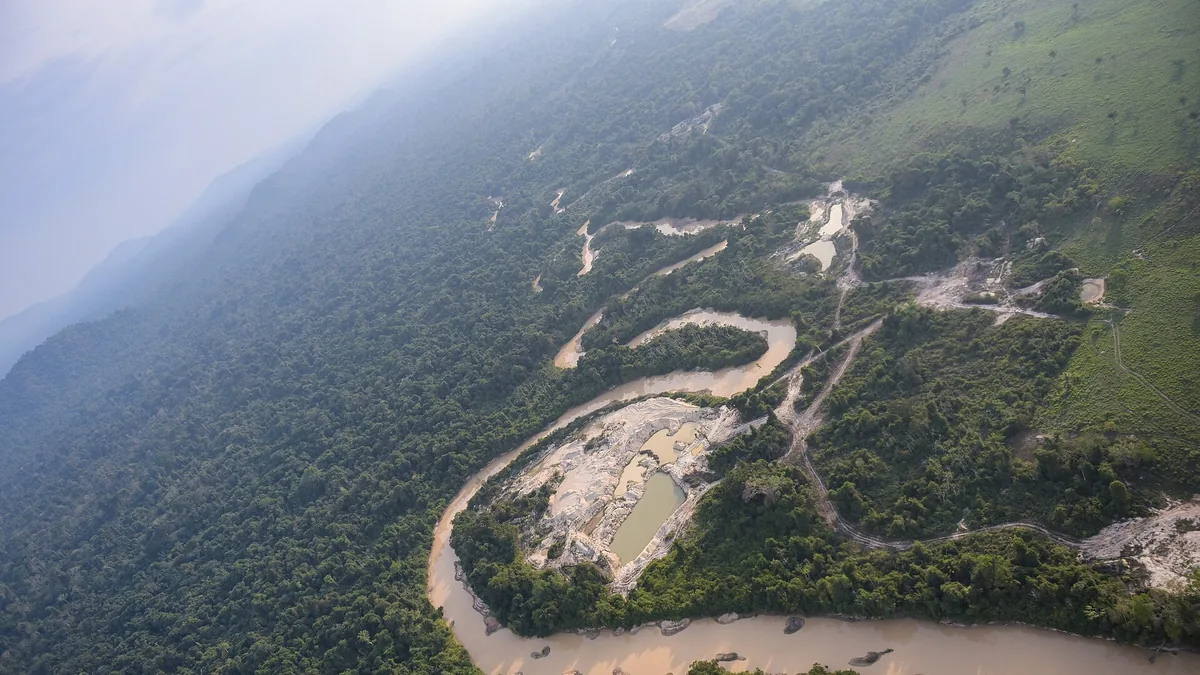 Vista aérea de una gran mancha de tierra removida por la minería junto a un río de aguas turbias, rodeada de selva